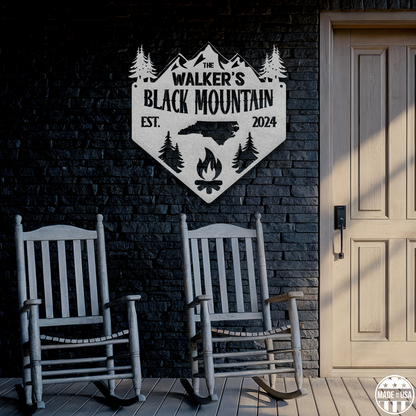 A customizable metal sign is mounted on a brick wall. Beneath the sign are two comfy rocking chairs ready for you!