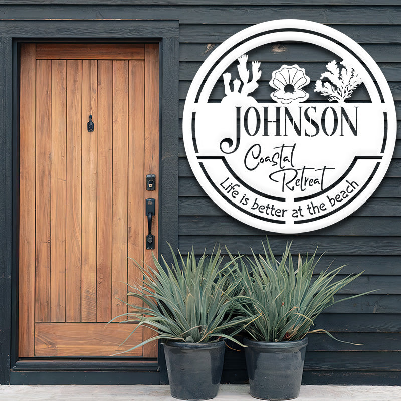 White metal sign on the exterior of a house, plants underneath, and a wooden door.
