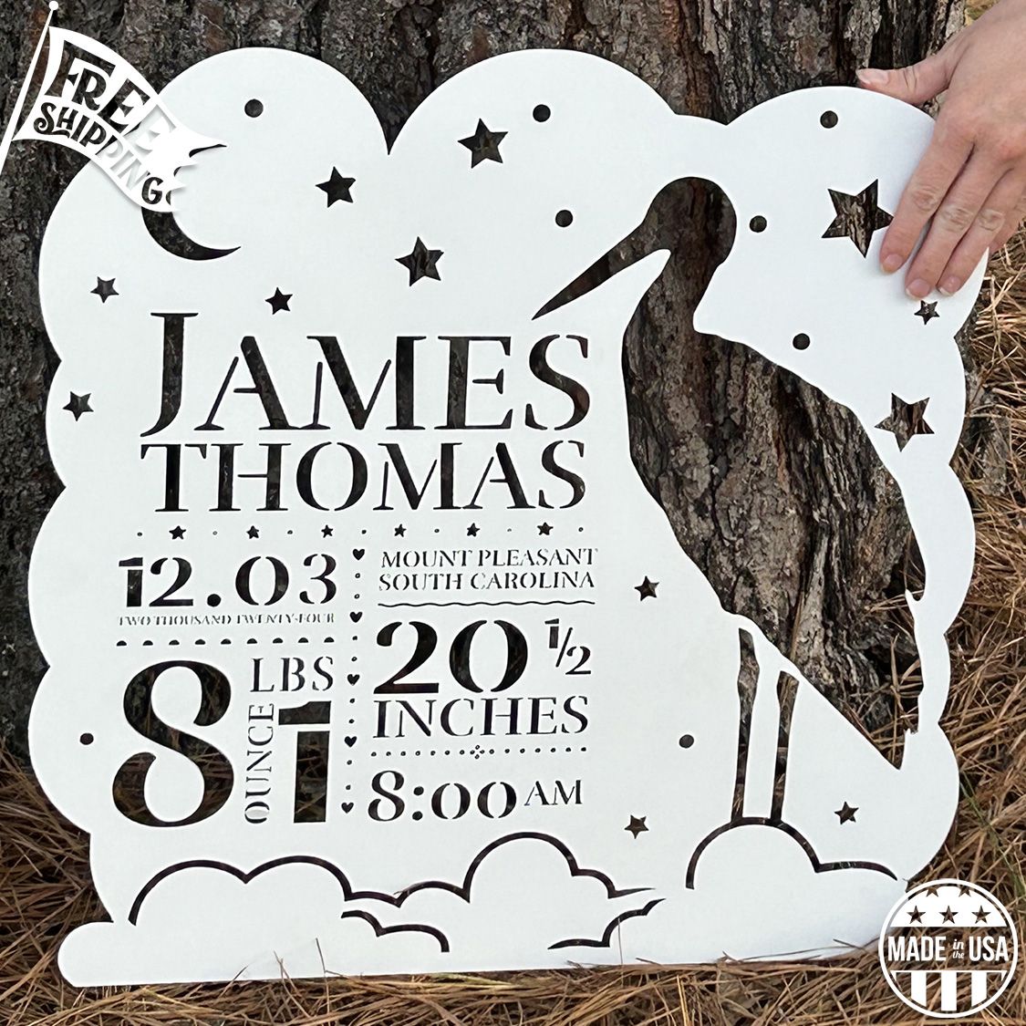 Personalized metal wall art with stork and baby design against a tree trunk.