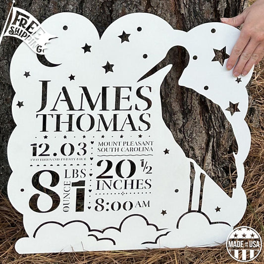 Personalized metal wall art with stork and baby design against a tree trunk.